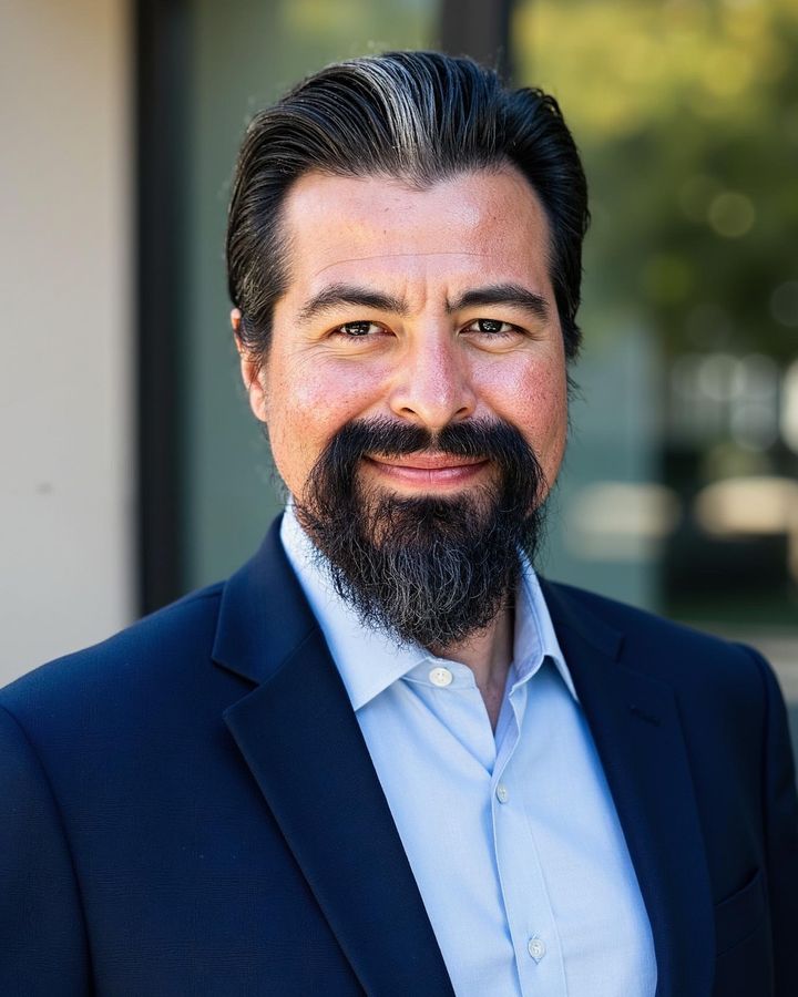 Portrait of Hector Villicana, smiling, wearing a navy blazer and light blue shirt outdoors.